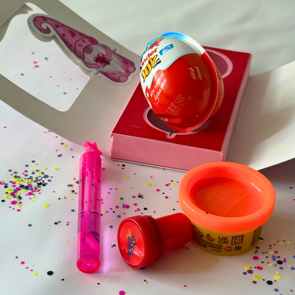 Red toy with colorful packaging on a white surface with confetti