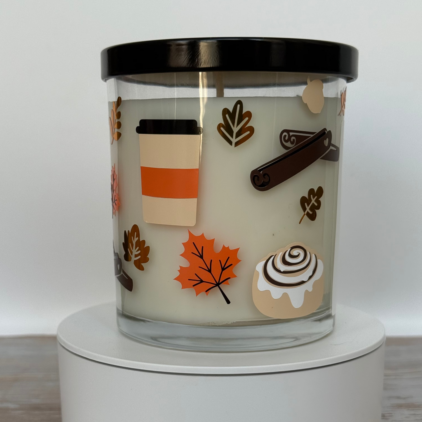 Candle with autumn-themed illustrations on a white surface