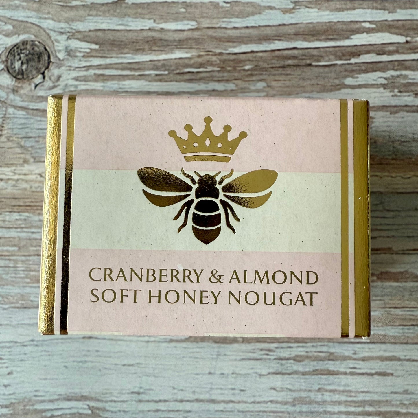 Box of cranberry and almond soft honey nougat with a bee and crown design on a wooden background