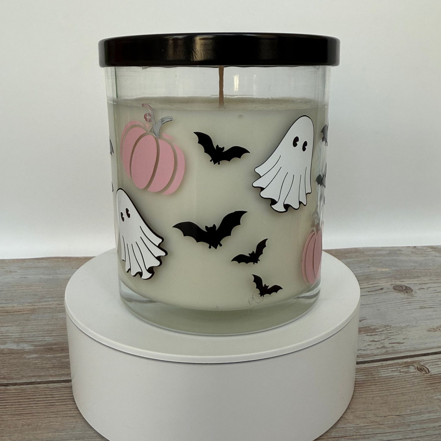 Halloween-themed candle with pumpkins, ghosts, and bats on a white base.