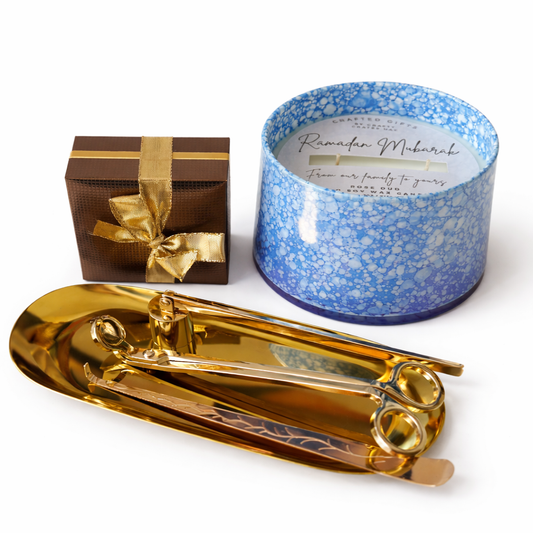 Gold scissors and a gift box with a blue speckled candle on a white background