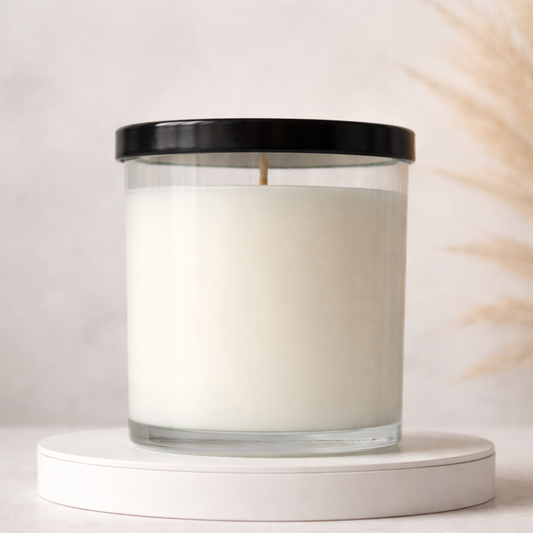 White candle in a glass jar with a black lid on a white platform against a light background