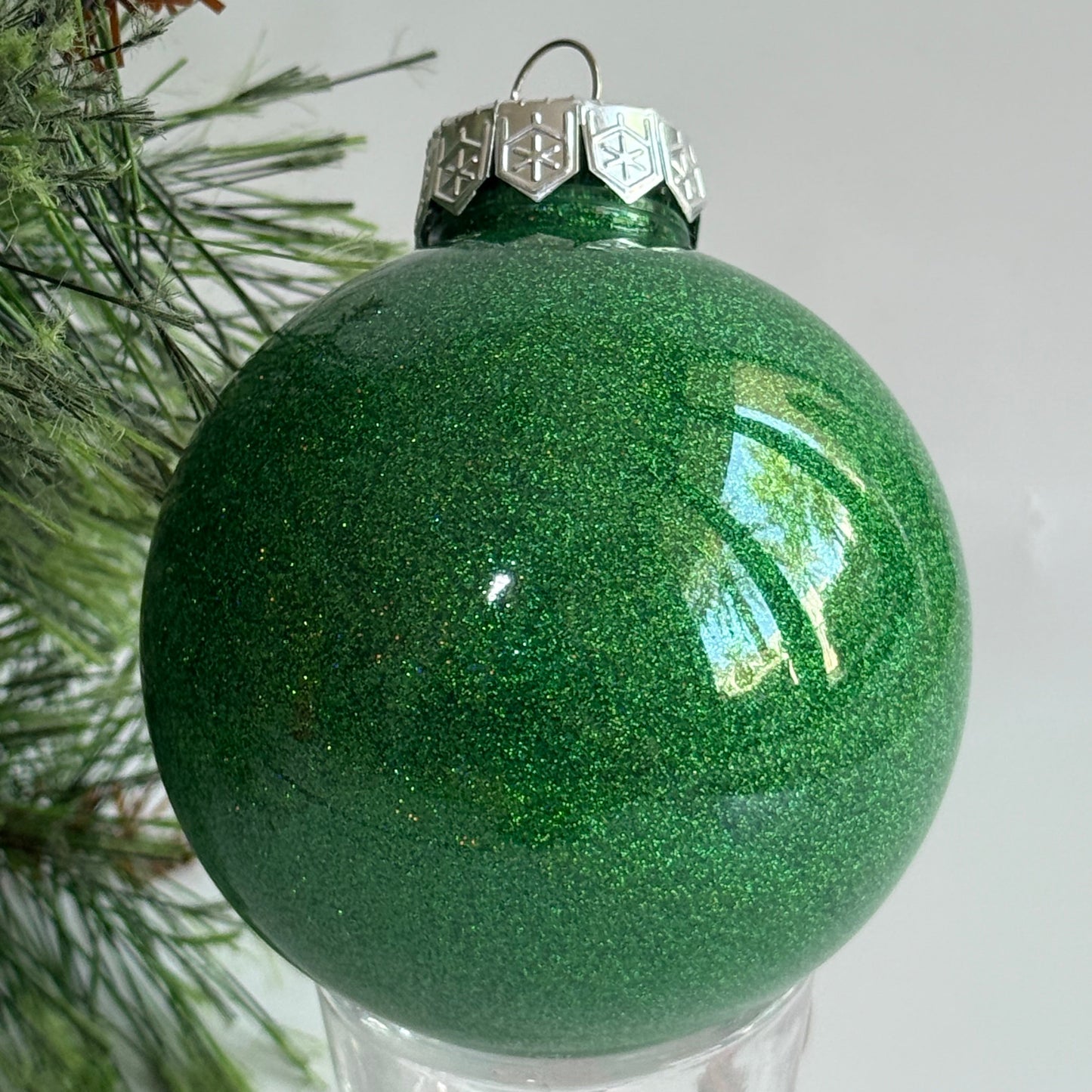 Green glittery Christmas ornament on a tree branch with a white background
