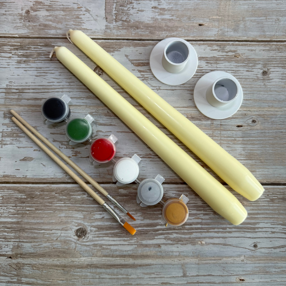 Two long yellow candles with candle-making supplies on a wooden surface