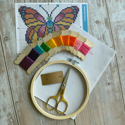 Embroidery hoop with colorful thread, scissors, and cross-stitch pattern on a wooden surface