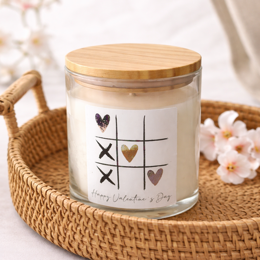 Candle in a glass jar with a wooden lid on a woven tray with flowers in the background