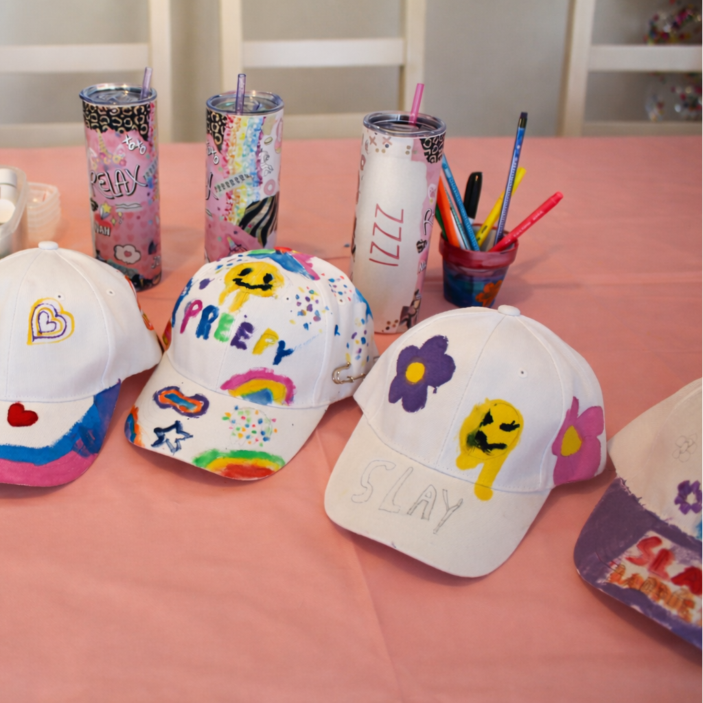 Colorful decorated baseball caps on a pink tablecloth with stationery items.