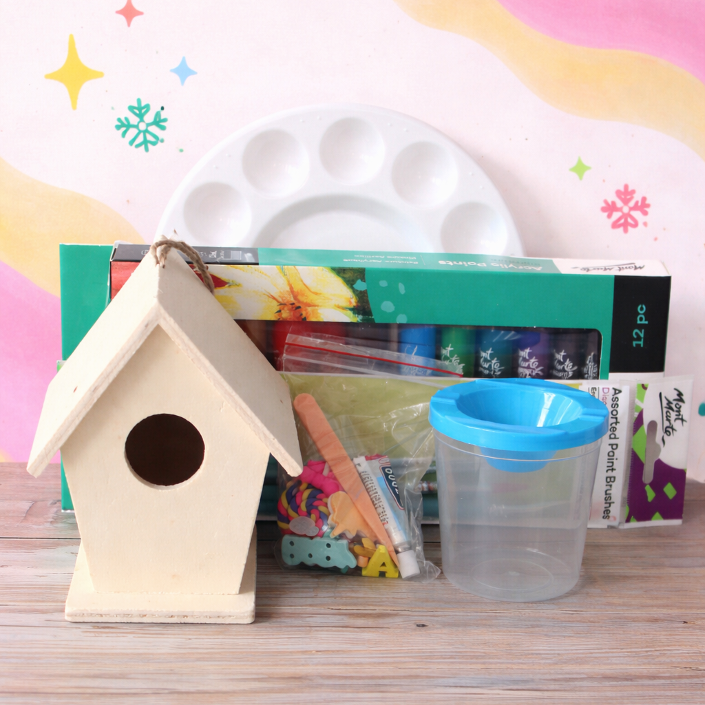 Small wooden birdhouse on a table with art supplies in the background