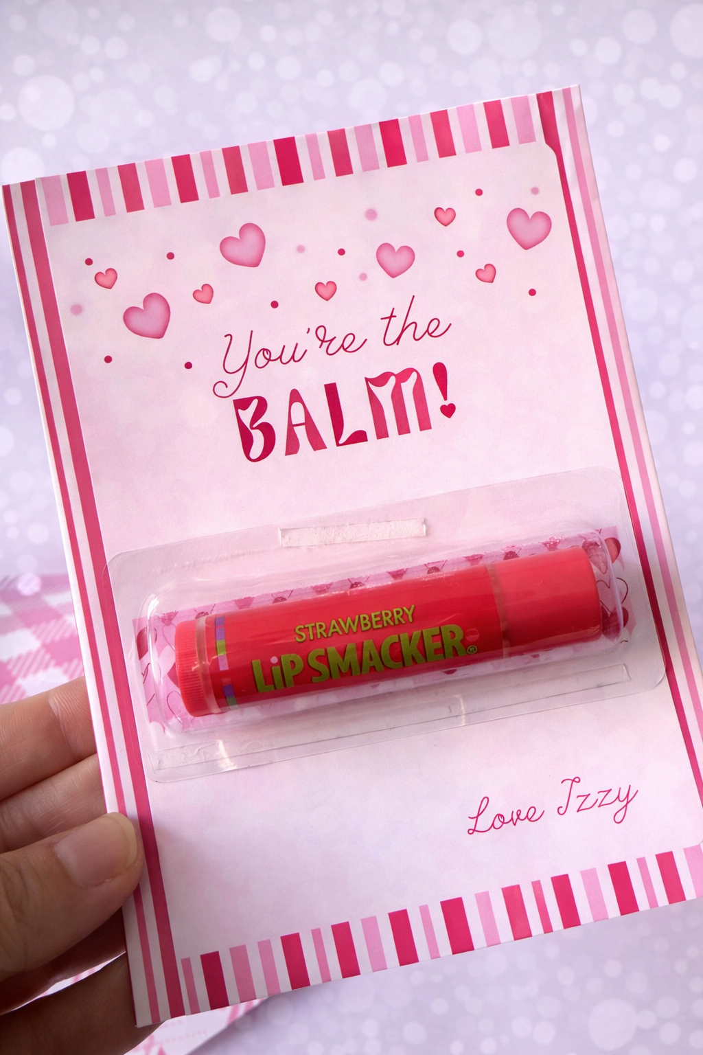 Lip balm in a decorative pink packaging with heart designs and text.