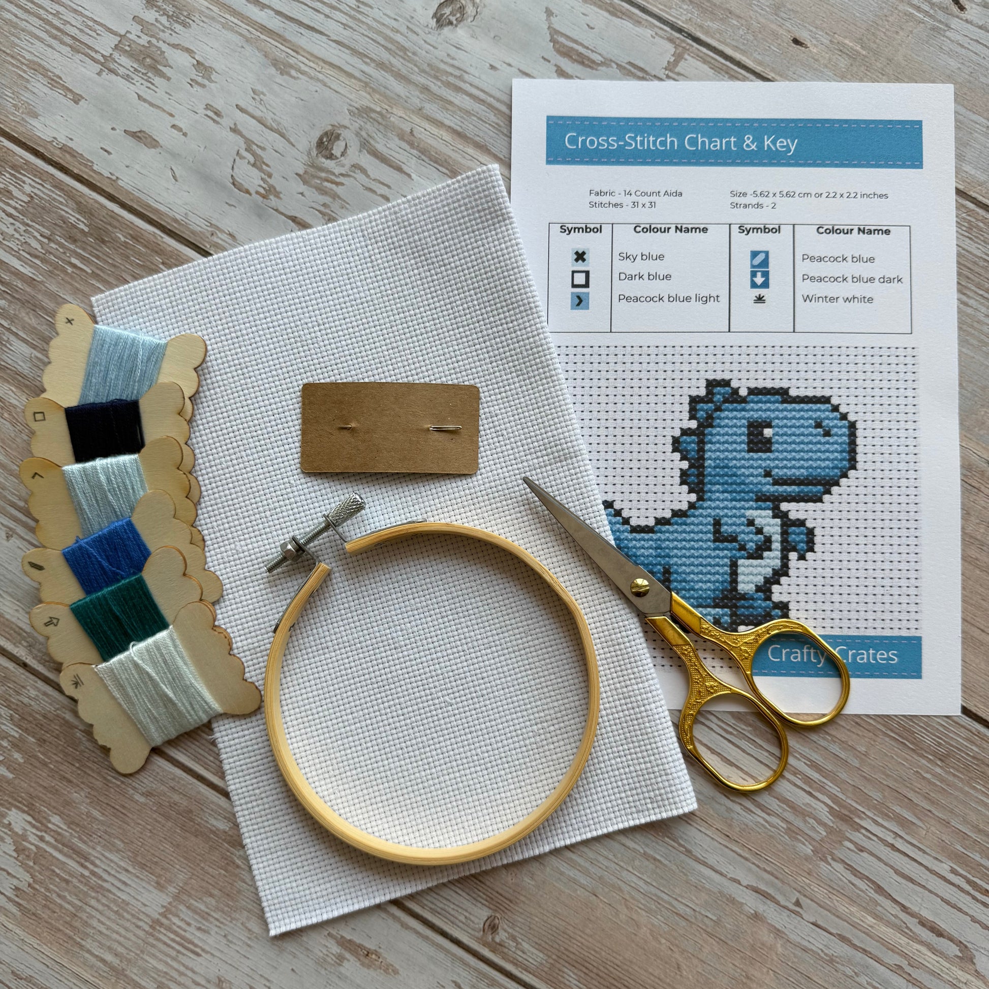 Embroidery hoop, scissors, and cross-stitch chart on a wooden surface