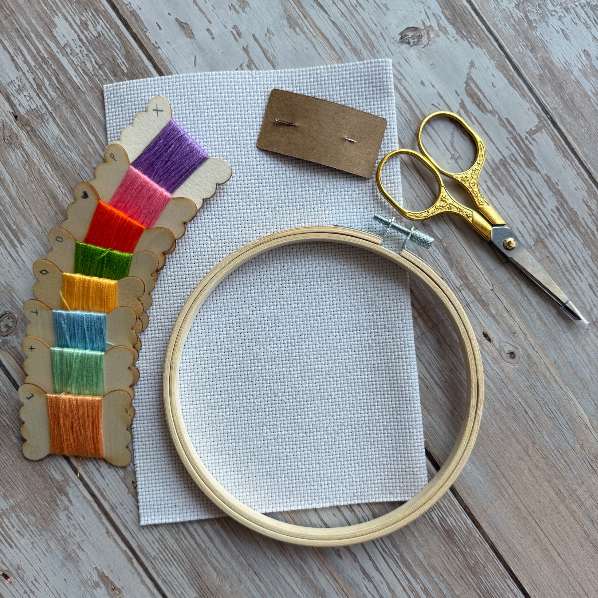 Embroidery hoop with colorful threads, scissors, and fabric on a wooden surface