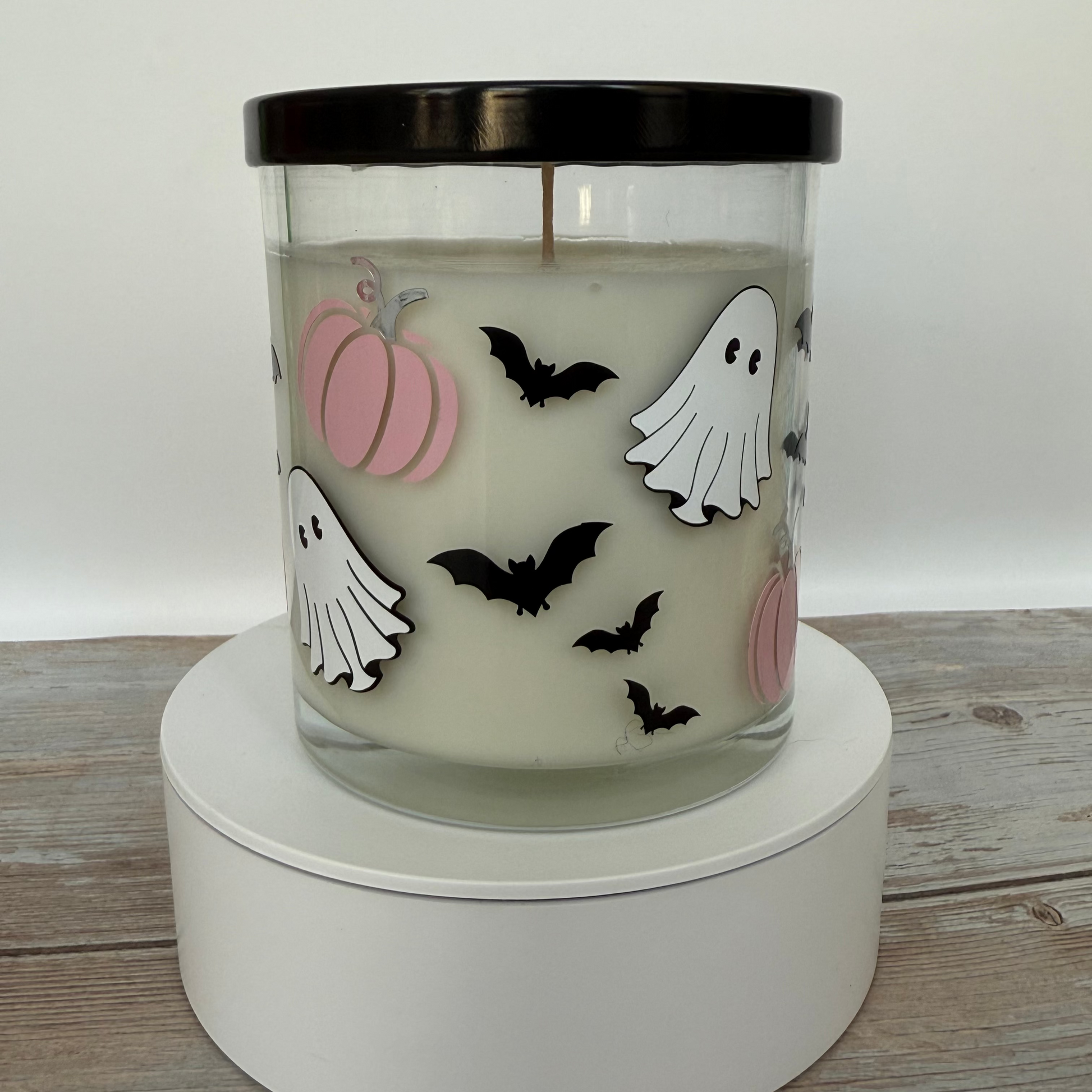 Halloween-themed candle with pumpkins, ghosts, and bats on a white base.