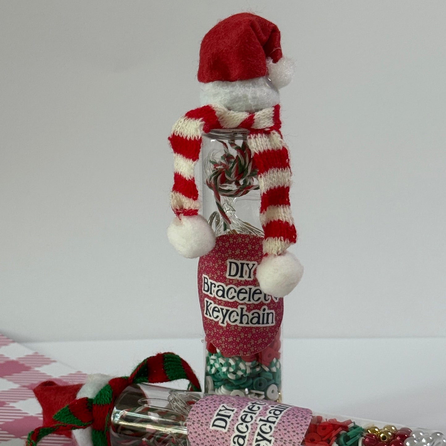 Red and white striped sock with pom-poms, a clear tube of decorative items, and a pink label on a white background.