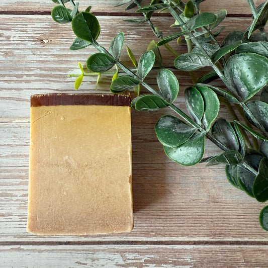 Gold bar of soap on a wooden surface with green leaves