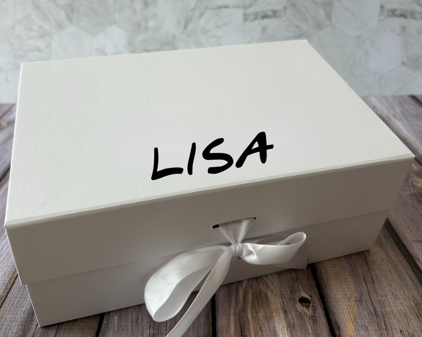 A white gift box with the name printed on the lid, adorned with a white ribbon and a bow.