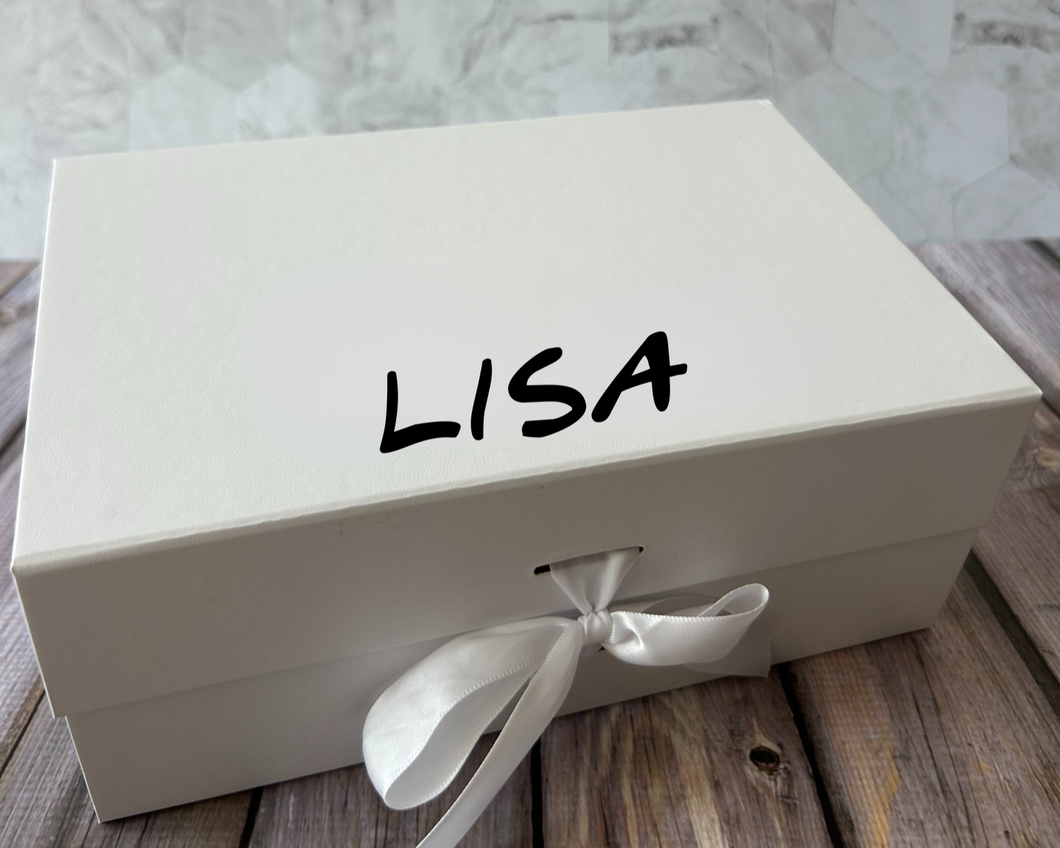 A white gift box with the name printed on the lid, adorned with a white ribbon and a bow.