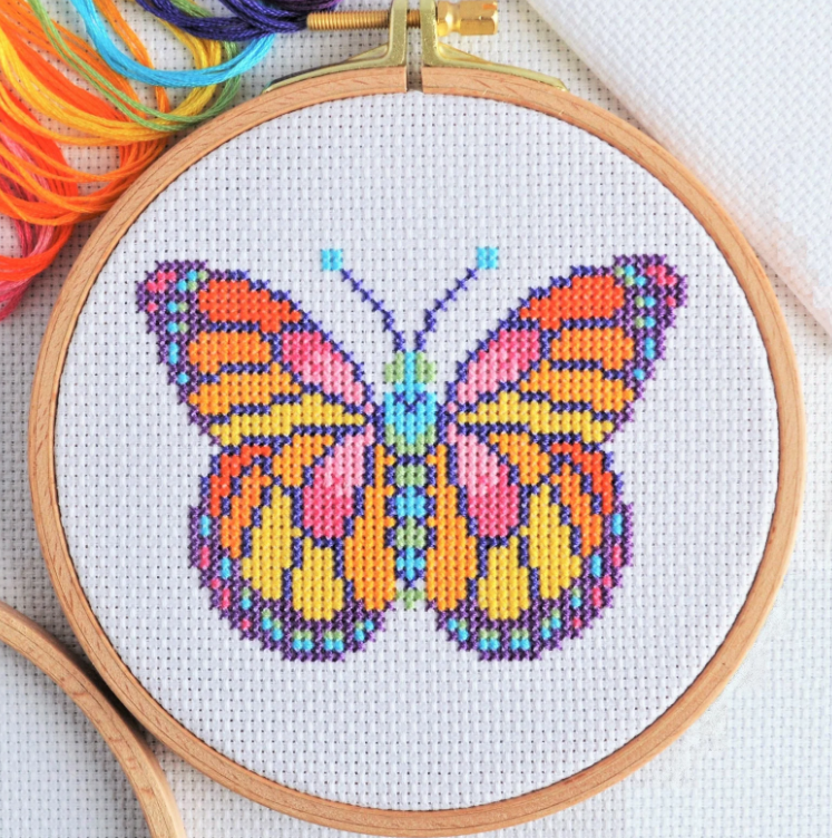 Cross-stitched butterfly design in an embroidery hoop with colorful threads.
