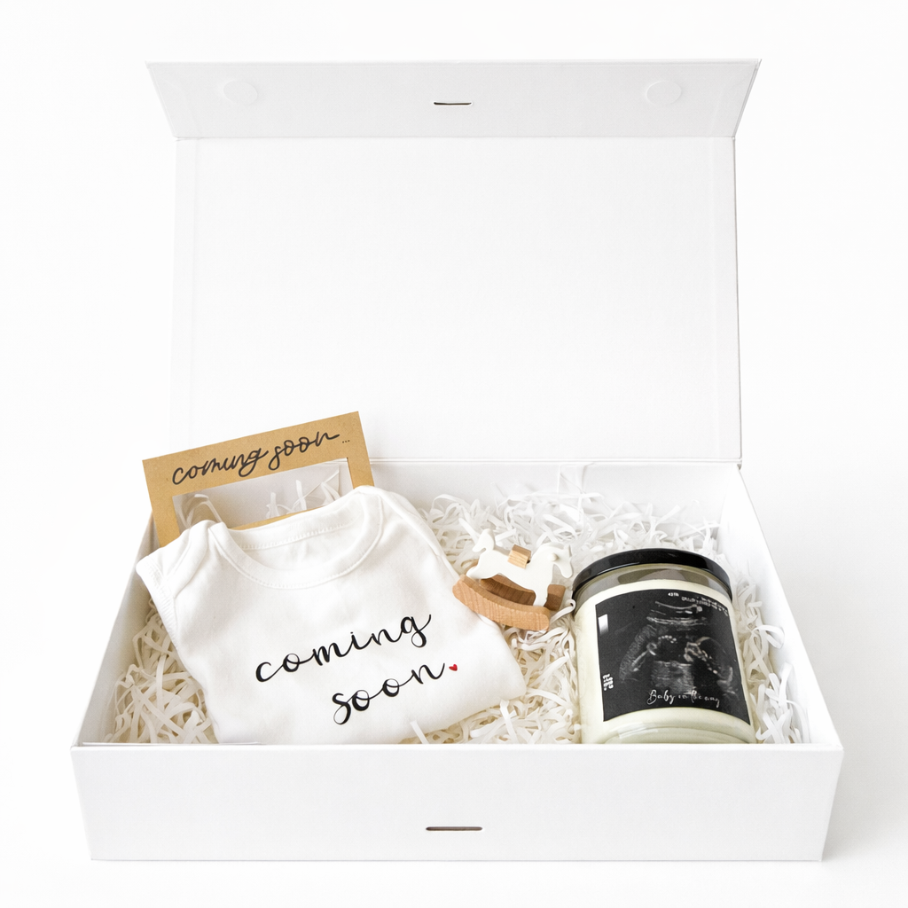 Gift set with a  candle, frame, baby onesie and rocking horse decoration in a box on a white background