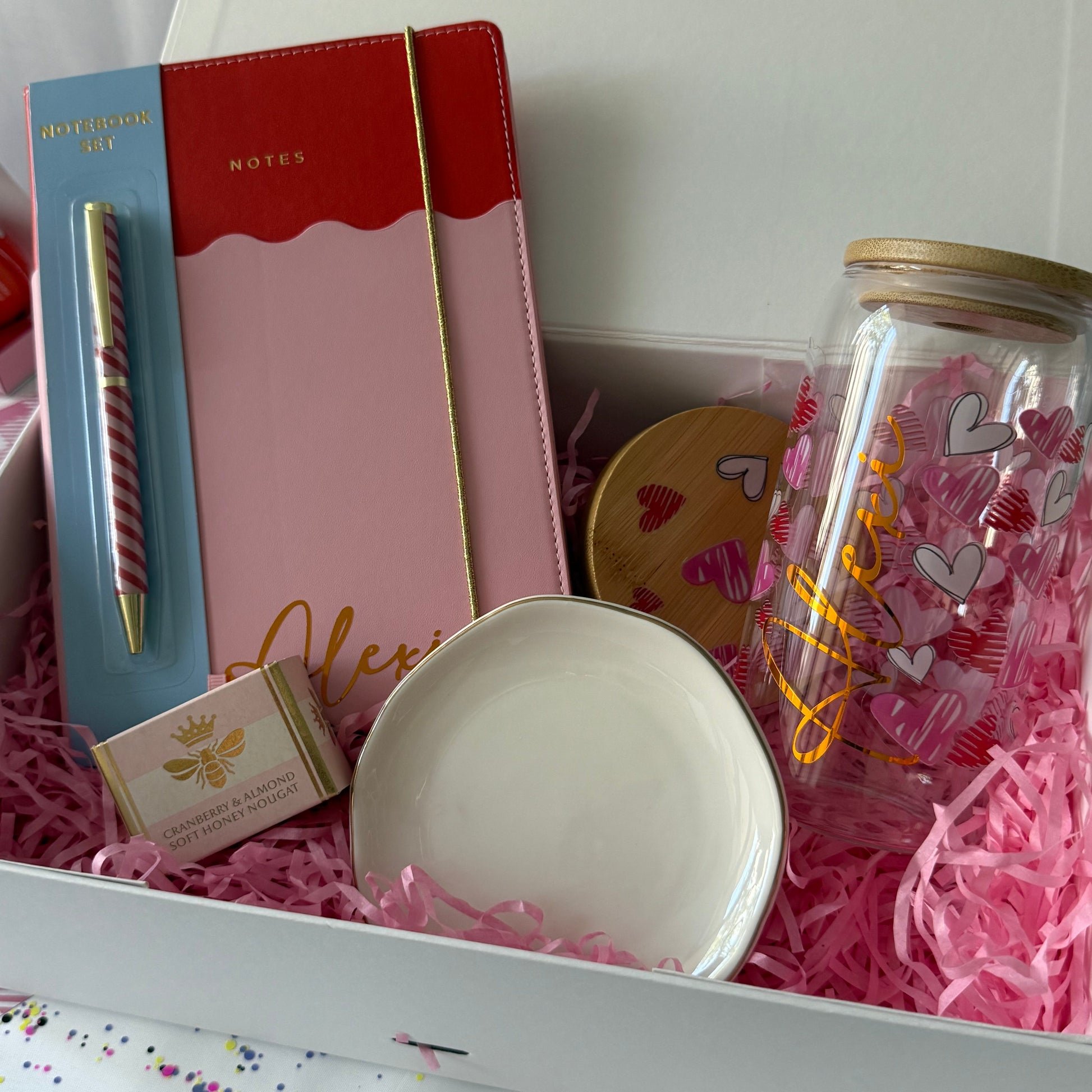 Gift set with a notebook, pen, and decorative jar on pink shredded paper.