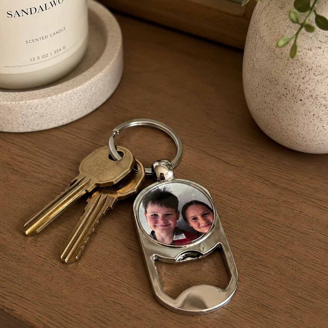Keychain with photo of two people on a wooden surface with a candle and plant in the background
