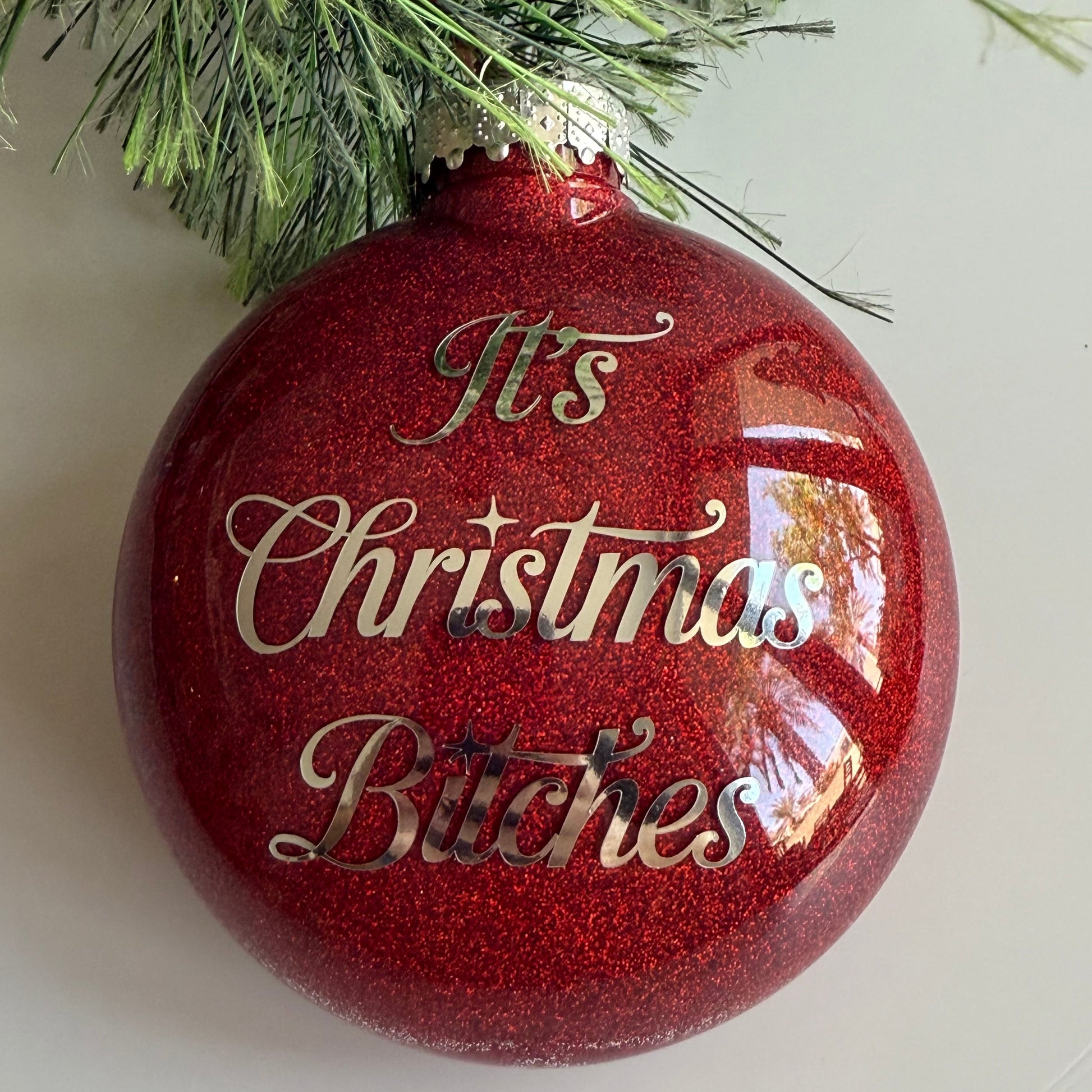 Red Christmas ornament with gold text 'It's Christmas Bitches' on a white background.