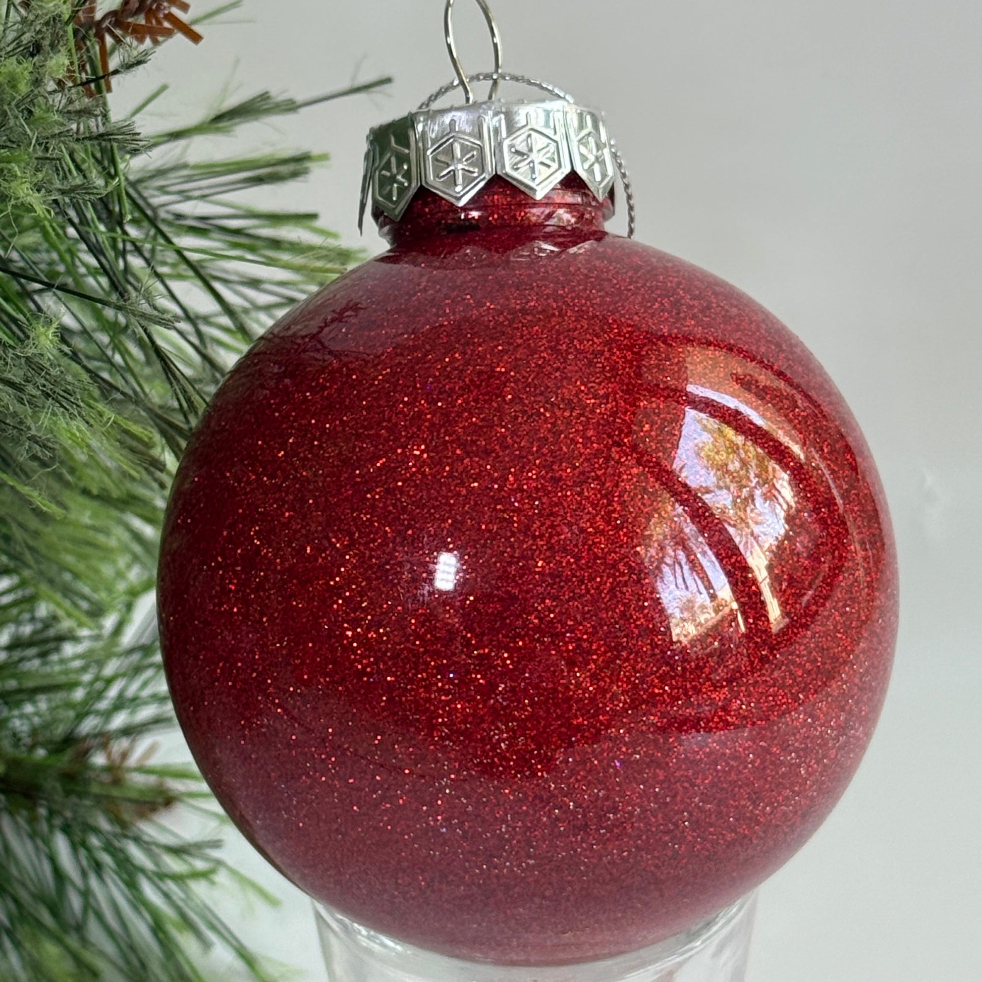 Red glittery Christmas ornament on a branch with a light gray background