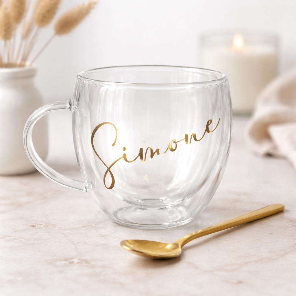 Clear mug with 'Simone' in gold script, gold spoon, and blurred candles in the background
