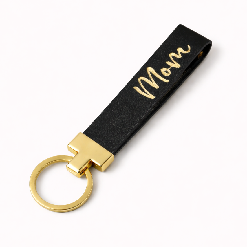Black leather keychain with gold lettering and ring on a white background