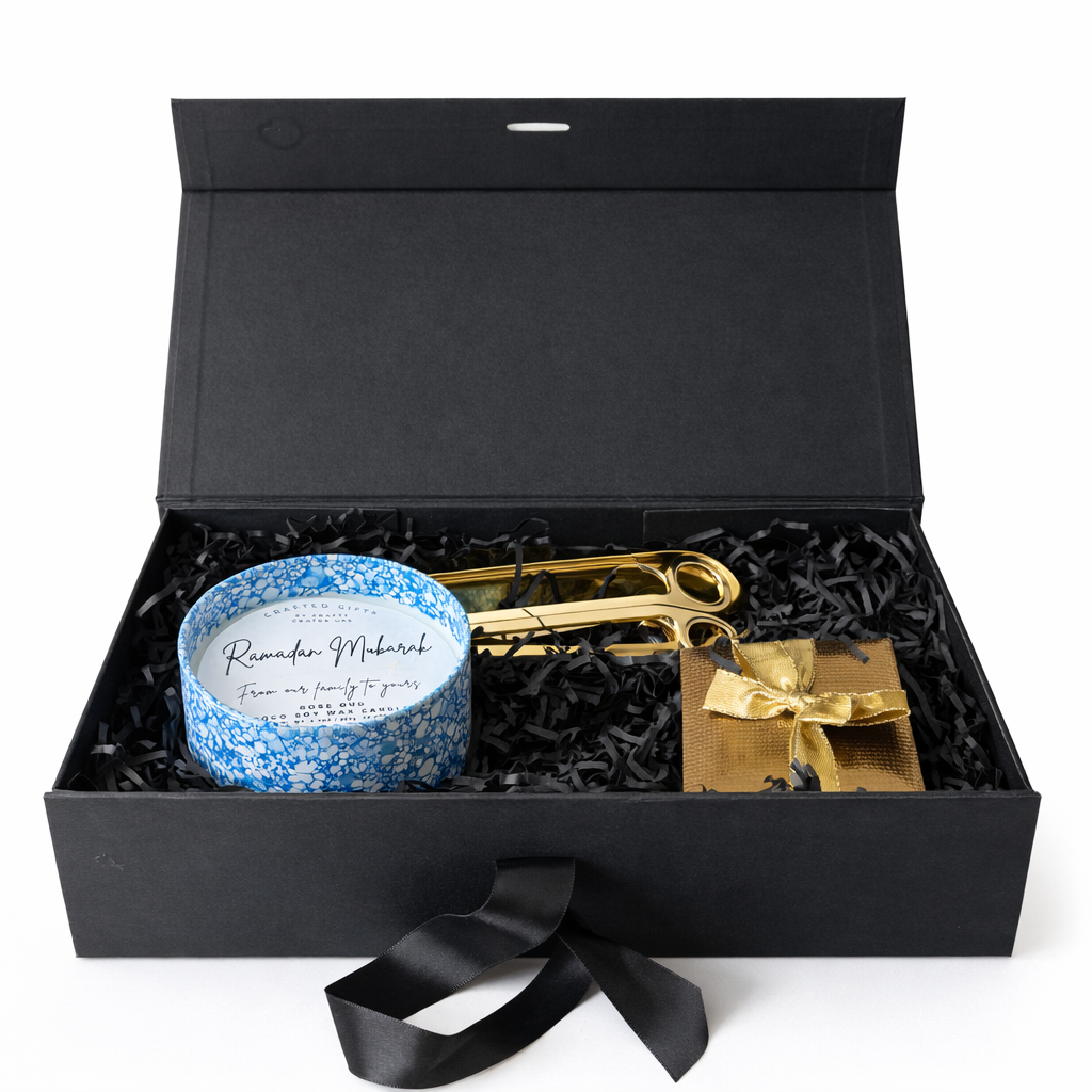 Gift box with a blue candle, gold scissors, and a gold bow on a white background